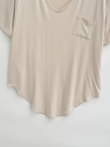 Detail of light beige V-neck short sleeve shirt featuring chest pocket and curved hem