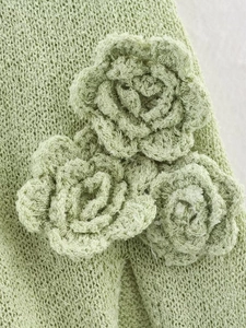 Détail du tissu en maille vert clair avec trois décorations de roses au crochet en 3D