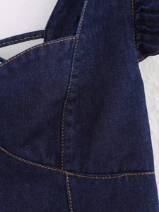 Detail of dark blue denim fabric featuring orange contrast stitching and ruffle trim