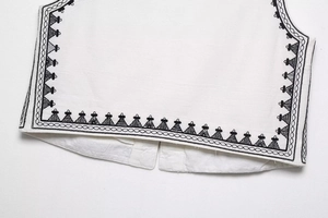 Detailed close-up of geometric embroidery on white vest hem with black wavy pattern