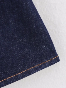 Close-up of deep blue denim hem with contrast orange stitching and twill fabric texture