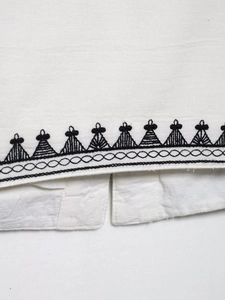 Detailed close-up of geometric black embroidery on white linen cotton fabric hem