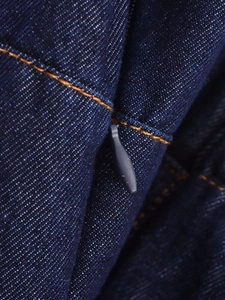 Detailed macro view of dark blue denim fabric with orange stitching and hidden zipper