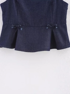 Close-up of slim fit dark blue denim top featuring peplum hem and bow details