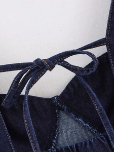 Detailed close-up of dark blue denim fabric with orange stitching and bow tie shoulder straps