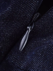 Macro shot of a high-quality metal zipper on dark blue denim fabric with neat stitching