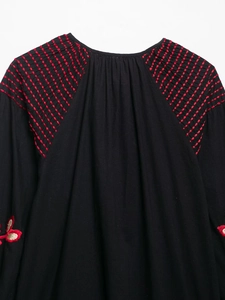 Détail de coutures rouges et broderies florales sur robe noire à manches longues
