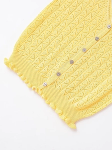 Détail de la veste en maille jaune avec texture ajourée, boutons perle et ourlet volant