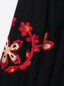Détail de broderie sur robe noire avec motifs floraux rouges et beige de haute qualité