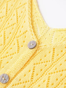 Détail du cardigan en maille ajourée jaune avec texture crochetée et bouton marbré