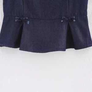 Sleeveless denim top with ruffled hem and bow accents in dark blue wash finish