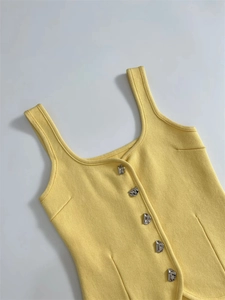 Close-up of light yellow knit vest featuring unique silver metal buttons and square neck