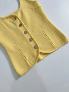 Close-up of yellow knit vest featuring textured fabric and irregular silver metal buttons