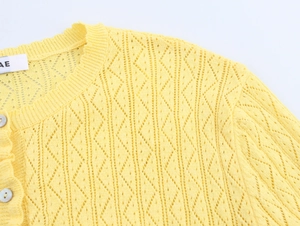 Close-up of hollow crochet knit pattern with pearl button details on yellow cardigan