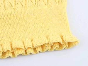 Detailed close-up of yellow knit fabric with openwork patterns and ruffled edges