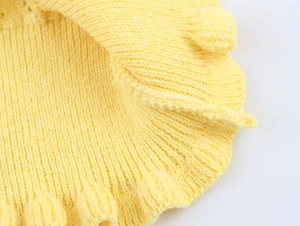 Detailed macro view of bright lemon yellow knit fabric texture and decorative pom-pom edges
