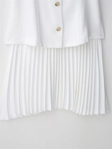 Detail of white dress featuring gold-colored buttons and refined pleated skirt fabric