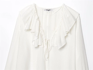 Detail view of white ruffled V-neck blouse featuring pleated texture and tie-up neckline
