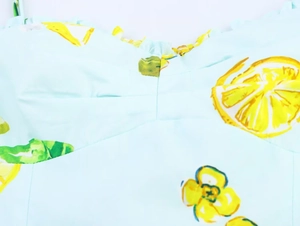 Detailed view of lemon print poplin fabric featuring pleated neckline and spaghetti straps