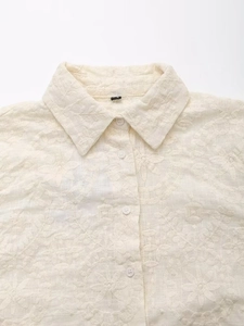 Détail d'une chemise crème en broderie anglaise avec col classique et boutonnage