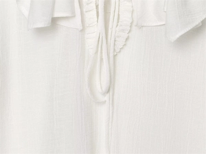 Close-up of white blouse featuring ruffled neckline and adjustable drawstring detail