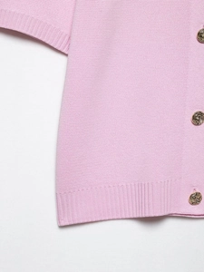 Gros plan sur un cardigan en maille rose avec des boutons dorés à texture spirale