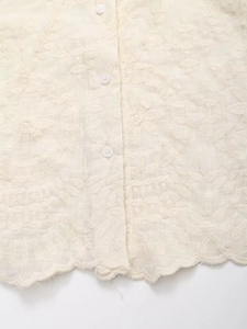 Détail du chemisier en broderie anglaise crème avec boutons et ourlet festonné