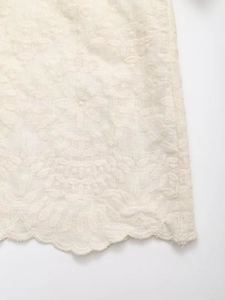 Détail du tissu en coton crème avec broderie florale et bords festonnés ajourés