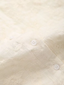 Détail de broderie jacquard florale et boutons blancs sur une blouse beige soyeuse