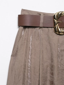 Detail of high waisted satin pants with metallic texture and a vintage brown belt buckle