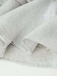 Macro detail of silver sequined fabric with metallic shimmer and overlock hem stitching
