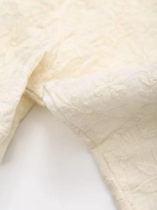 Détail de broderie florale blanche et motif ajouré sur tissu en coton couleur ivoire