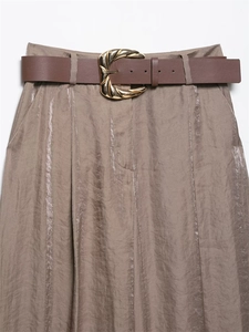 Detailed close-up of high-waisted satin trousers with a gold swirl buckle and leather belt