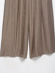 Detailed view of the wide-leg cut and glossy satin texture of the dark brown trousers