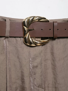 Detail of a golden twisted metal buckle on a brown leather belt with satin trousers