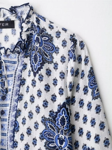 Detailed close-up of blue paisley print on white fabric with ruffled neckline and ties
