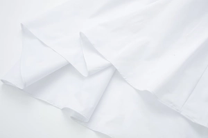 Close-up of white poplin midi dress fabric showing multi-layered pleated hem and stitching