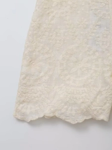 Détail de broderie en coton blanc avec motifs floraux et finition bord festonné