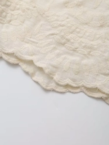 Vue macro de broderie florale délicate sur coton crème avec détail de bord festonné