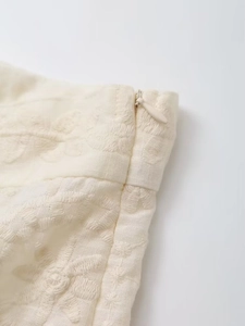 Vue détaillée du vêtement beige avec broderie florale 3D et fermeture éclair invisible