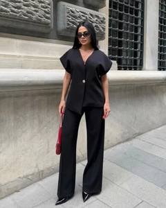 Détail du haut noir à col en V avec bouton doré et pantalon assorti à jambes larges