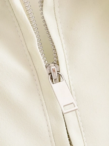 Macro shot of silver metal zipper on cream-colored twill fabric with textured detail