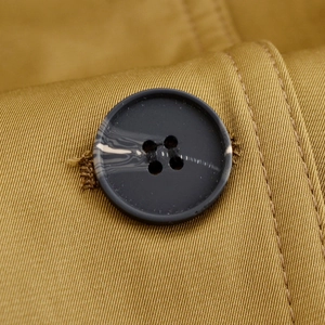 Close-up of marble texture button on minimalist mustard yellow pilot jacket twill fabric
