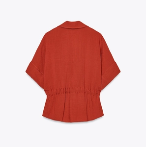 Detail of brick red short sleeve shirt showing elastic waist and linen-like texture