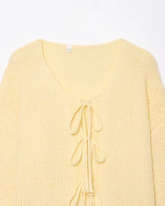 Close-up of pale yellow knit cardigan featuring delicate bow ties and soft texture