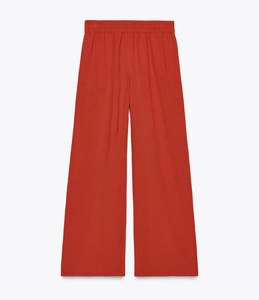 Detail view of rust red wide-leg trousers with elastic waistband in linen fabric