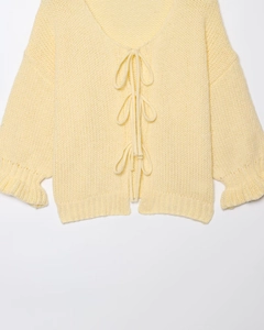 Close-up of light yellow knit cardigan featuring front ties and ruffled sleeve cuffs