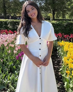Detail of white V-neck dress with decorative front buttons and cinched waist in a garden