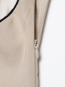 Detail of invisible zipper on beige midi dress with black piping and woven texture