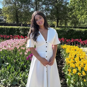 Detail of white V-neck dress with black buttons and cinched waist in a tulip garden